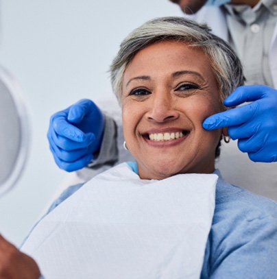 Woman smiling while holding handheld mirror in treatment chair