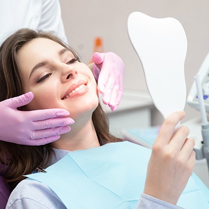 a patient admiring her smile in a handheld mirror