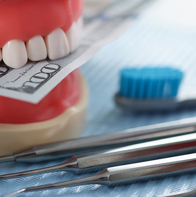 dental instruments sitting next to a plastic model of a mouth biting on money