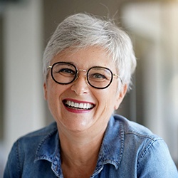 Senior woman with glasses smiling with dental implants in North Garland, TX 