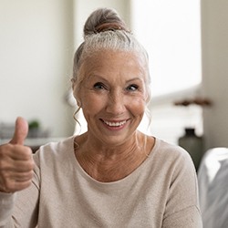 woman smiling and giving thumbs up after getting dental implants in Garland