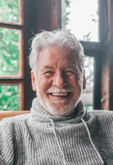 Older man with implant dentures in North Garland smiling at home