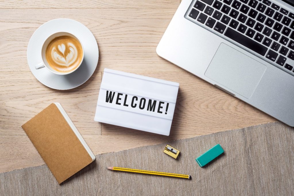 Welcome sign lying on desk with coffee, laptop, and notebook