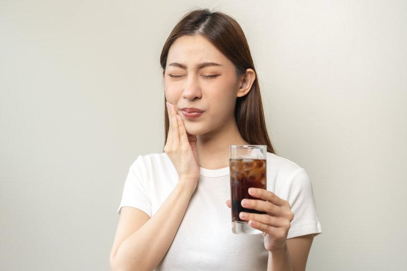 A woman feeling the negative effect of soda on teeth