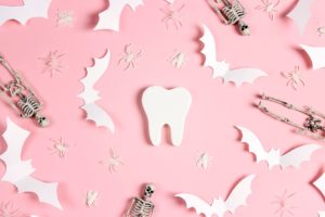 Toy spiders, white paper bats, toy skeletons, and a model of a tooth on a pink background