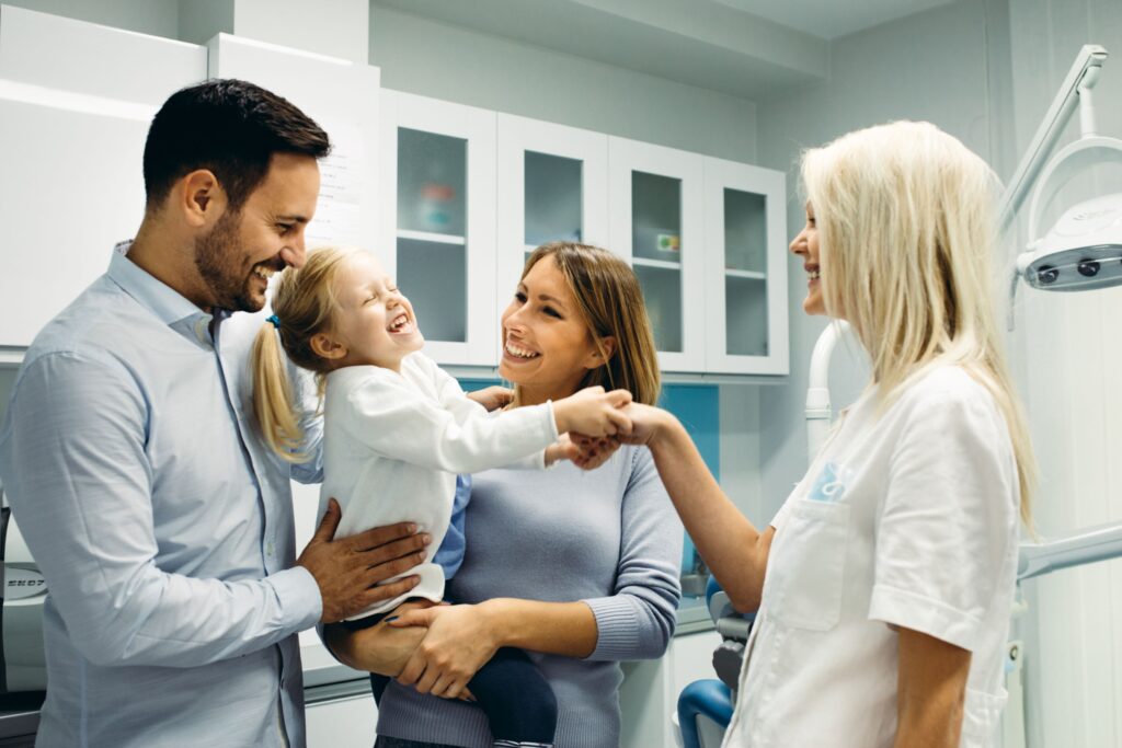 Little girl held by parents shaking dentist's hand