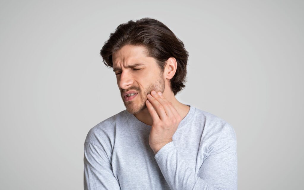 Man in gray shirt touching jaw in pain
